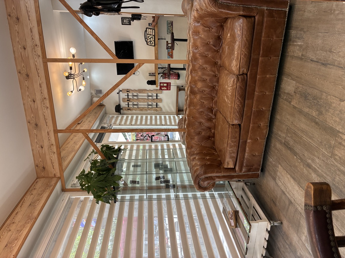 Zona de espera sofá Chesterfield cuero y madera barbería premium Barcelona